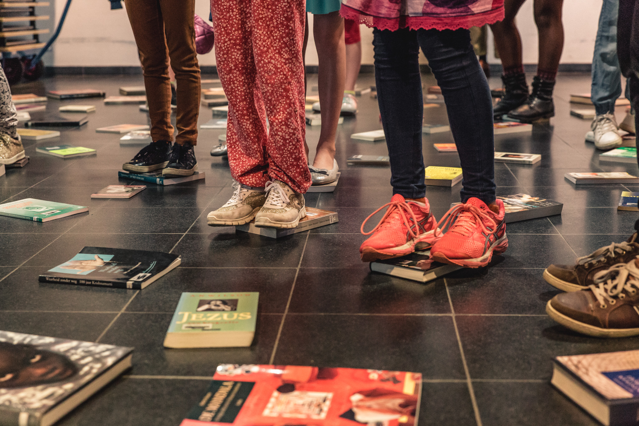 Tal van boeken liggen op de grond, kinderen kiezen hun favoriet door voorzichtig op het boek te gaan staan