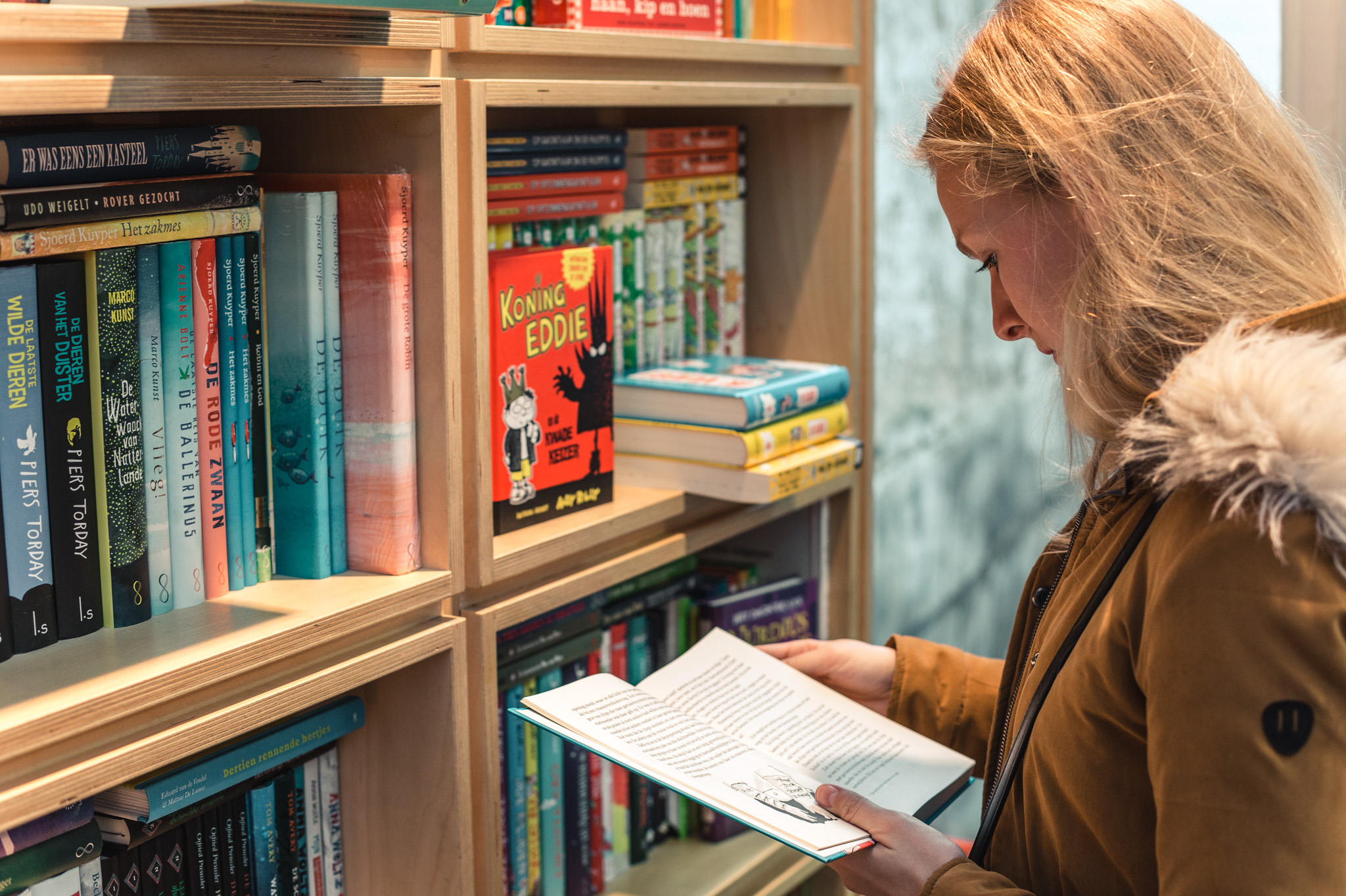 vrouw staat voor boekenkast en bladert door een boek