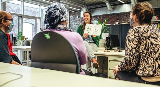 een lesgeefster leest voor aan volwassenen in het volwassenonderwijs