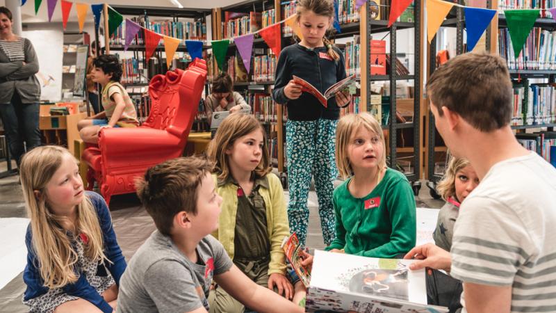 kinderen luisteren naar auteur in de bibliotheek