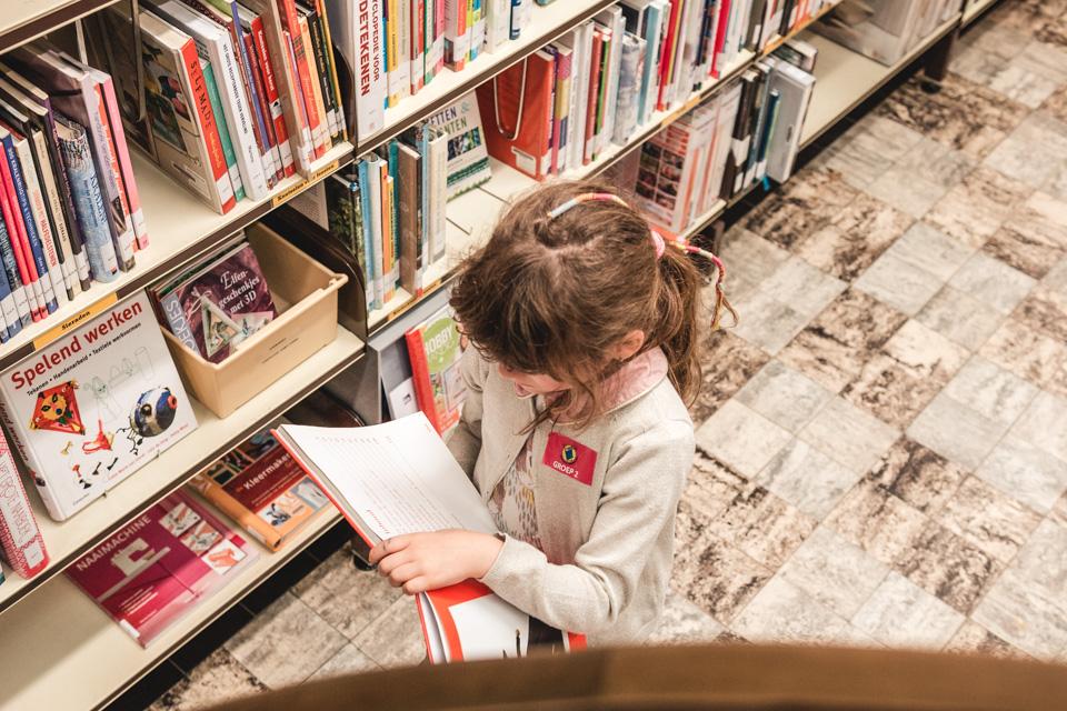 Meisje kiest een boek uit een boekenkast