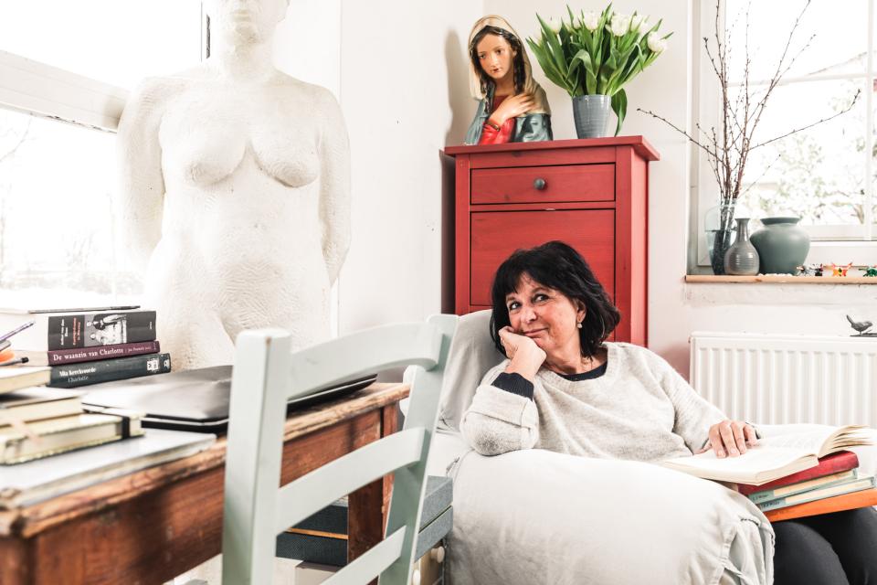 Auteur Kristien Dieltiens zit rechts in de zetel met boeken op haar schoot. Links liggen op tafel haar favoriete boeken.