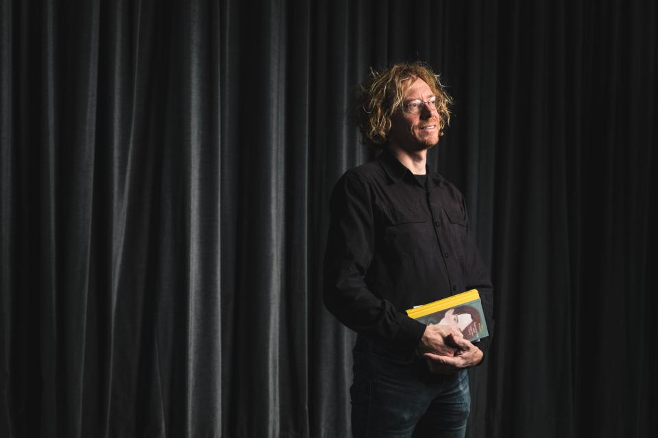 portret van Hendrik Vos die al rechtstaand een boek vasthoudt. de achtergrond is een donkergrijs fluwelen gordijn