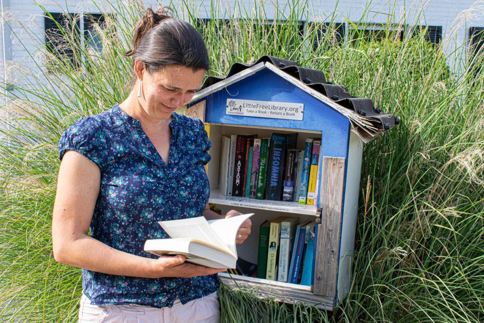 een eigenaar van een boekenruilkastje poseert naast haar kastje terwijl ze door een boek bladert