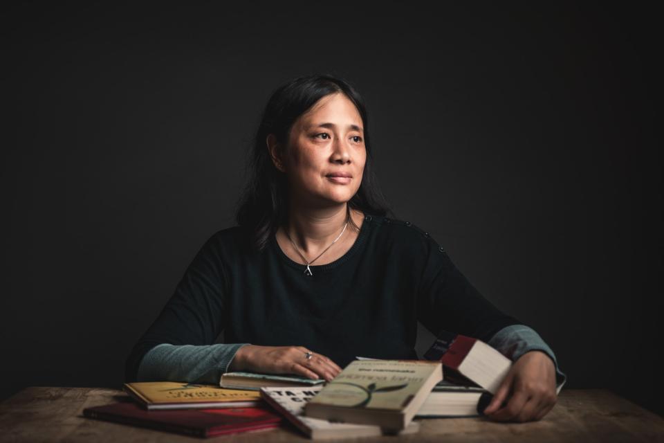 portret van winny ang die aan tafel zit. Voor haar liggen boeken verspreid op tafel. De achtergrond is donkergrijs.