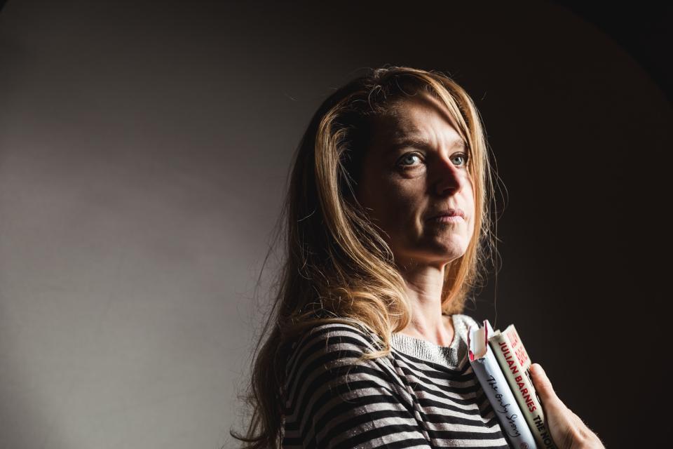 rika ponnet poseert voor de lens met haar favoriete boeken in haar armen. Ze kijkt weg van de lens. De achtergrond is effen, in grijs en zwart.