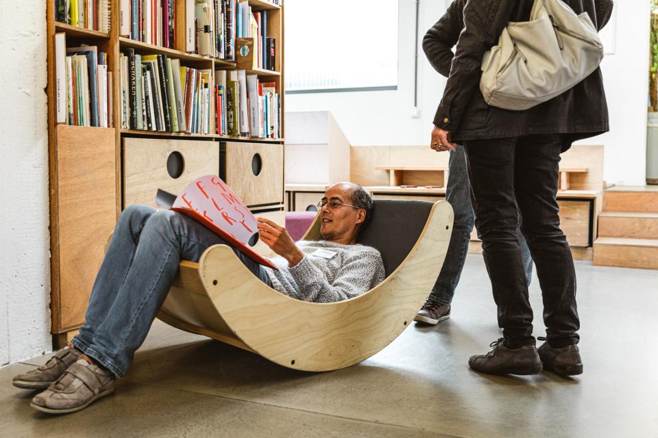 man zit een kinderboek te lezen in een houten schommelzetel - op de achtergrond staat een boekenkast